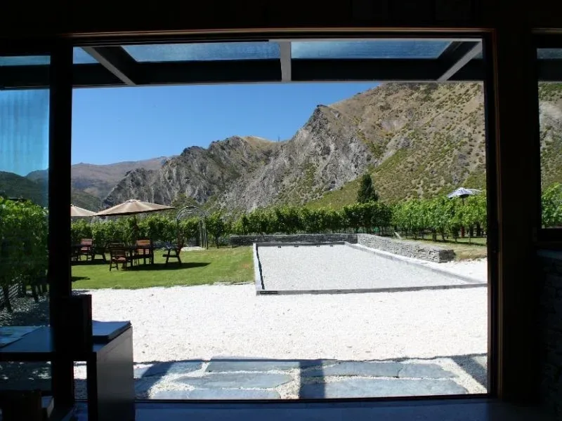 Looking out of the open tasting room doors across a gravel court and vine rows to the rock face beyond