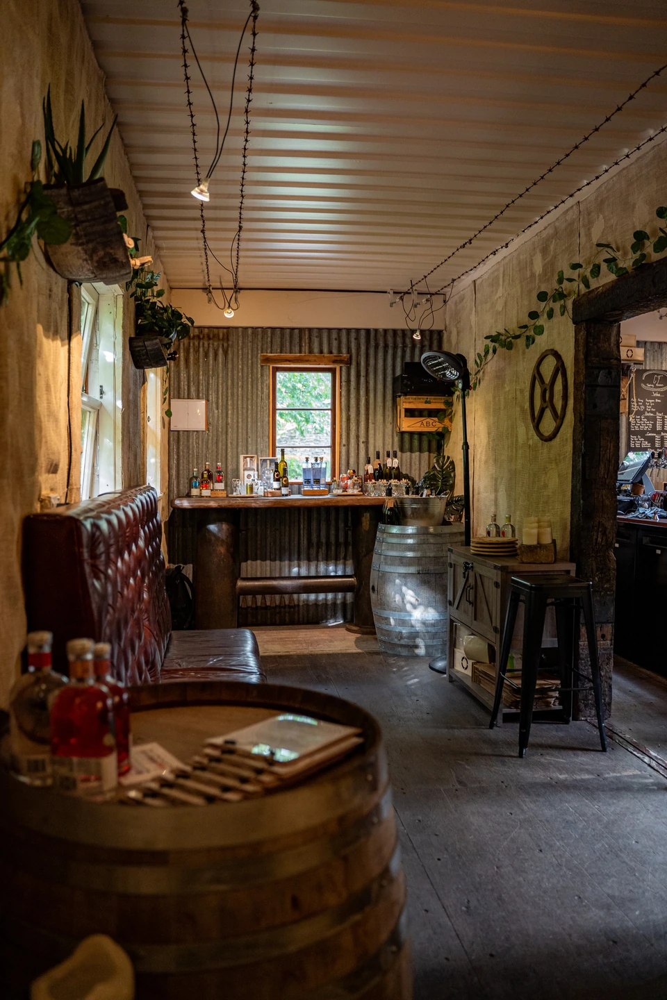 Inside the tavern: a leather booth, a wine barrel used as a table and a timber bar under a corrugated-iron ceiling