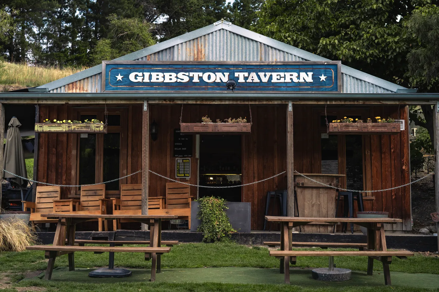 Timber and corrugated-iron pub front under a painted GIBBSTON TAVERN sign, with picnic tables set out on the grass
