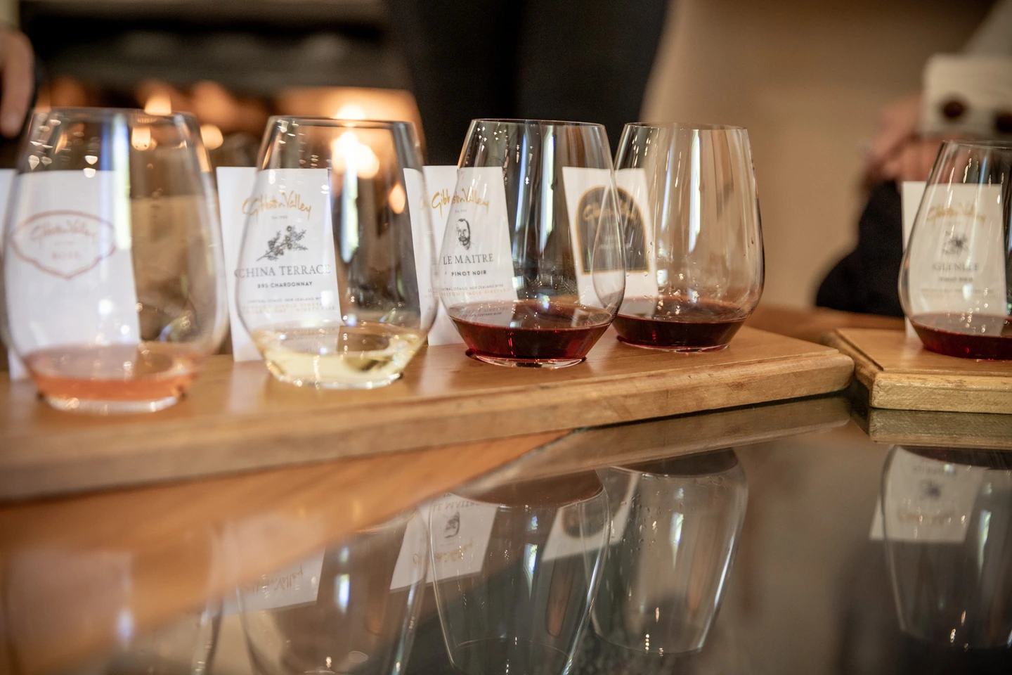 Six tasting glasses lined up on a wooden board at the Gibbston Valley cellar door bar, rosé and chardonnay through to pinot noir