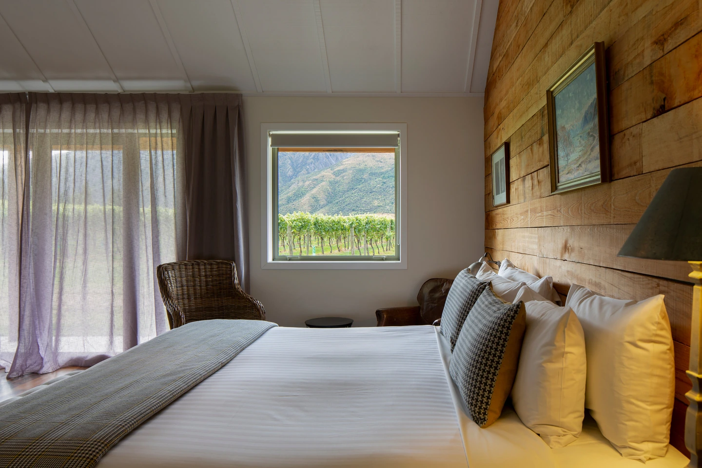A cottage bedroom with a timber-panelled wall behind the bed and vine rows visible through the window