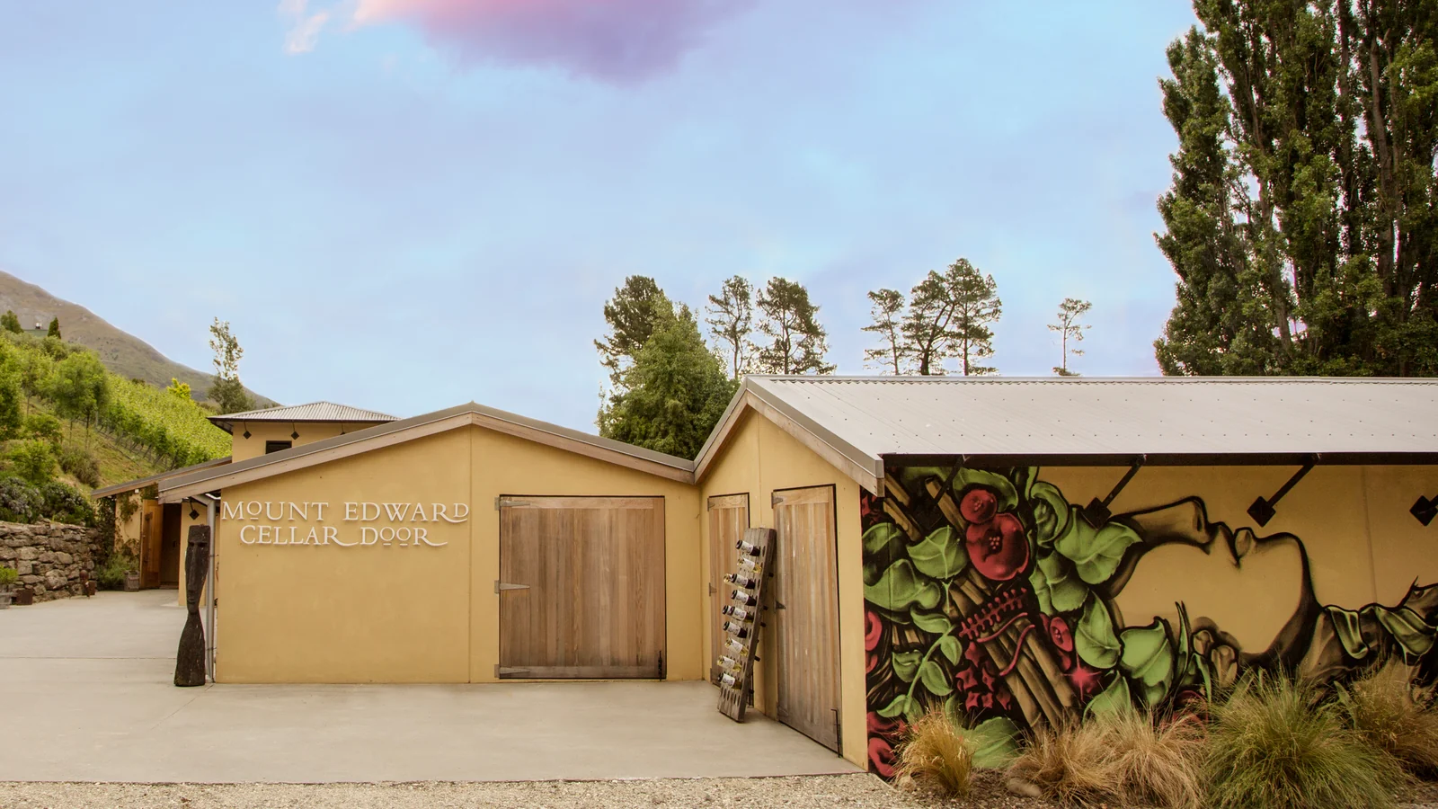 The Mount Edward cellar door buildings across a wide gravel forecourt, poplars and a vine-covered hillside behind