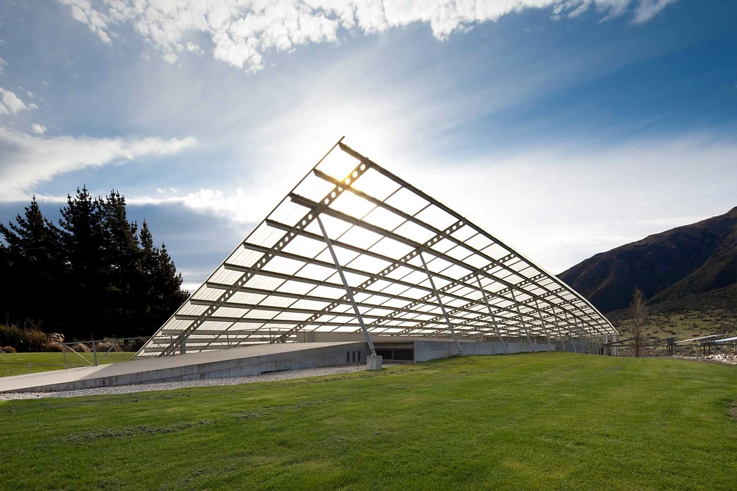 The winery's translucent canopy rising from the ground like a tilted wing, backlit by low sun with the Gibbston hills beyond