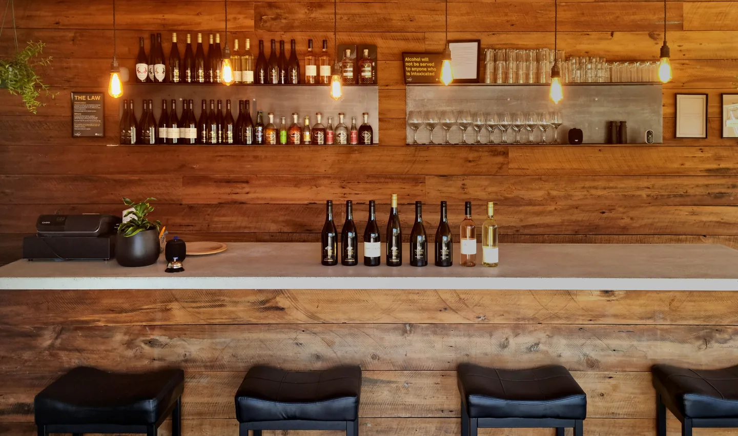 The timber bar inside the woolshed, bottles lined along the counter and shelves of wine, spirits and glassware behind